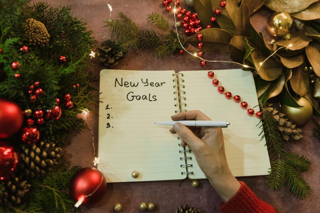 Hand writing New Year goals in a spiral notebook surrounded by festive Christmas decorations.